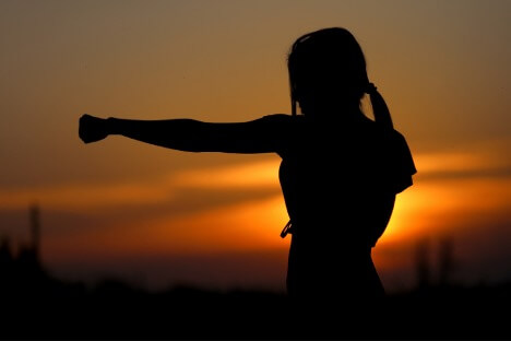A woman in a martial arts pose with a sunset