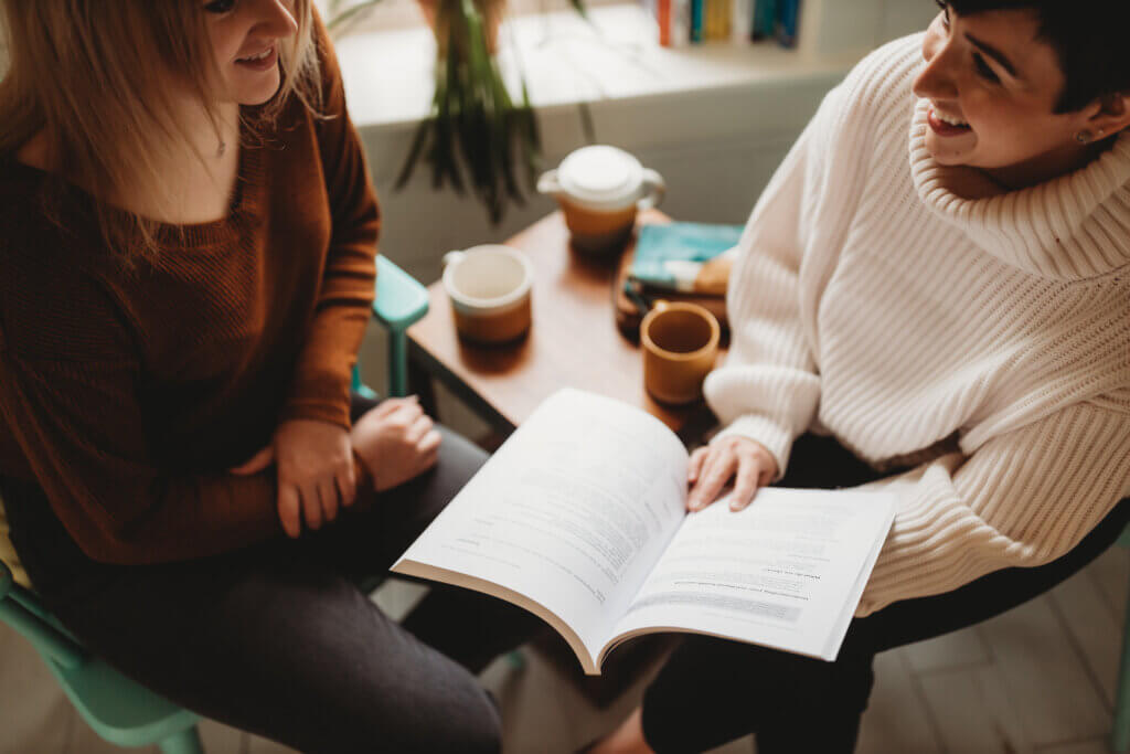 Image of two women talking, with one woman showing the other something in a book.