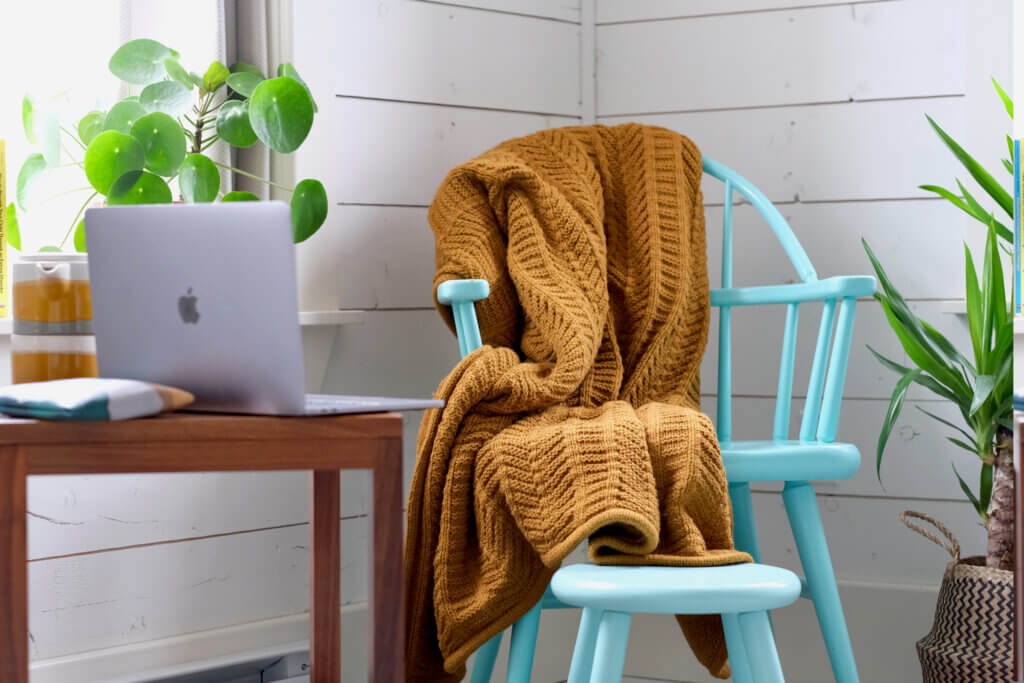 Chair with blanket on it next to side table with laptop.