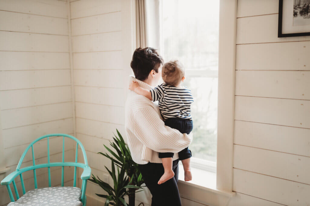 Jill holding her baby and looking out a window. 