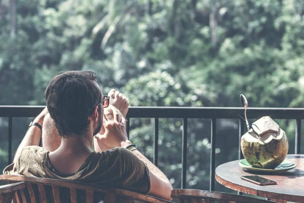 A man sits on a patio outside looking over nature.