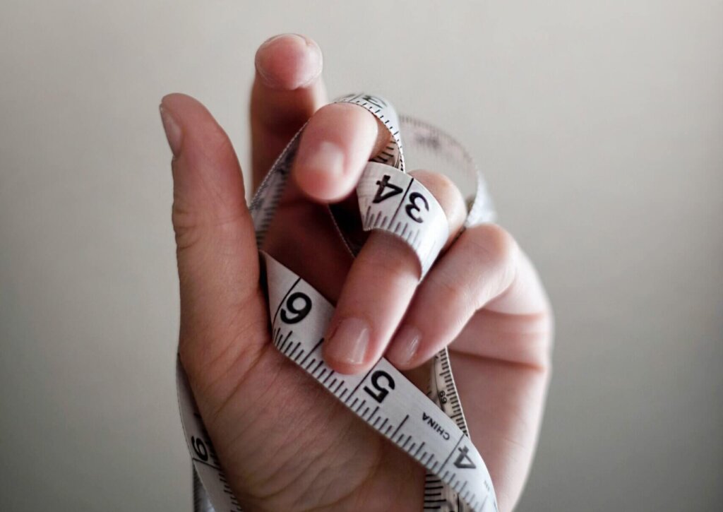 Hand with measuring tape around it against white background