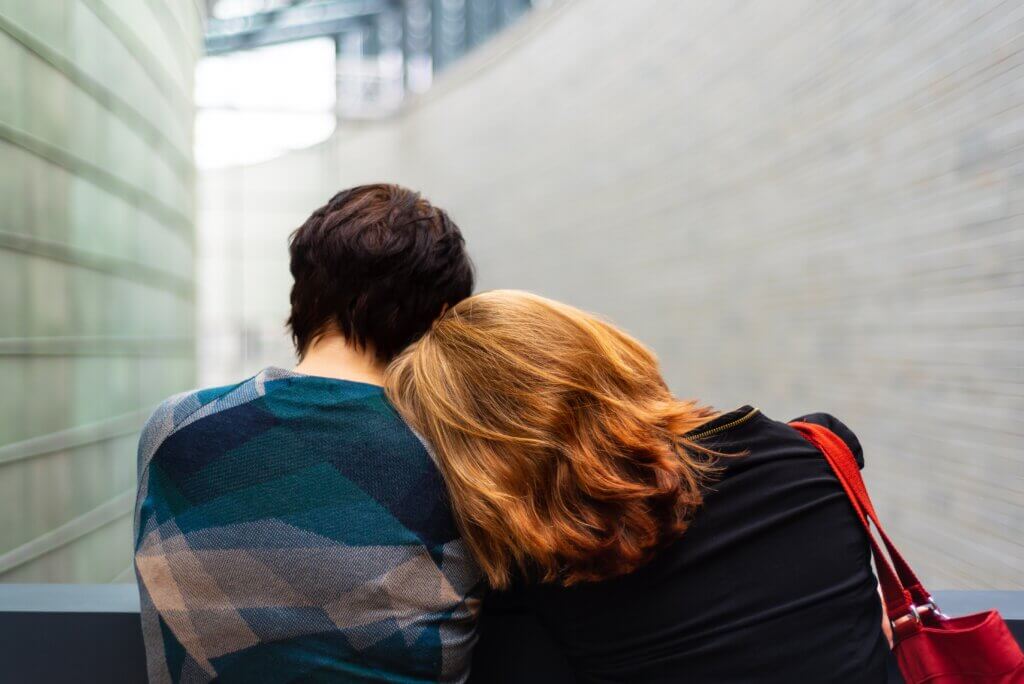 Two gender expansive individual sitting together, cuddled up.
