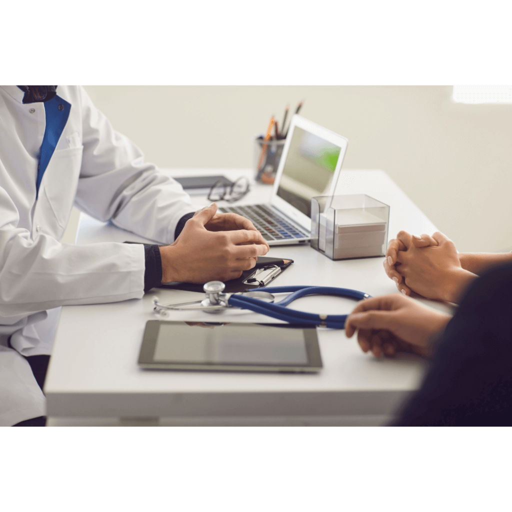 Doctor and patient sitting at desk that has a computer and stethoscope on it