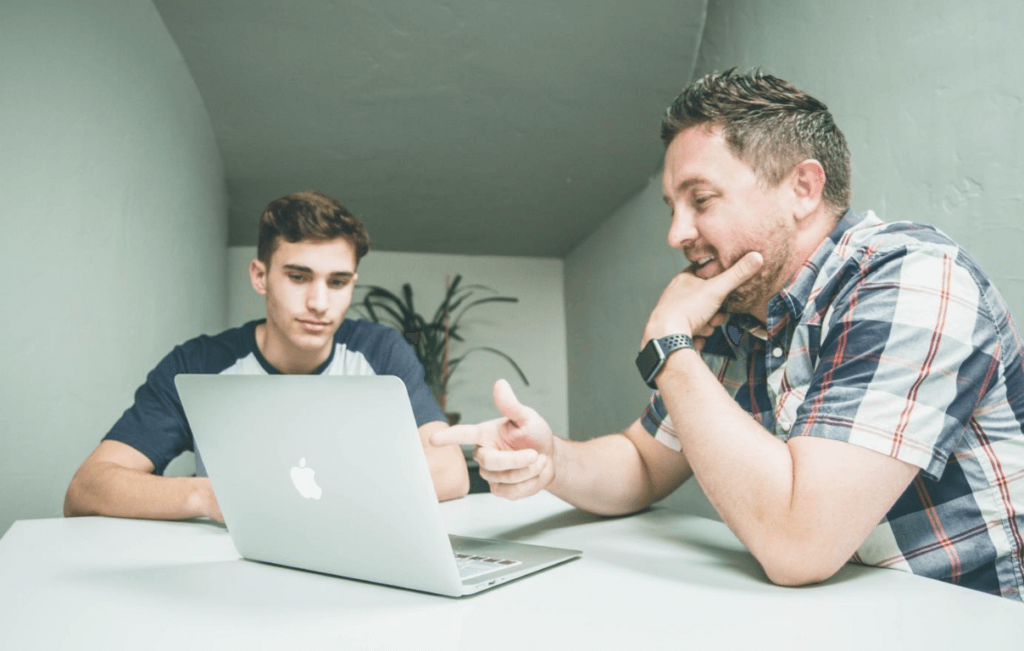 Two individuals sitting at a table looking at a laptop.
