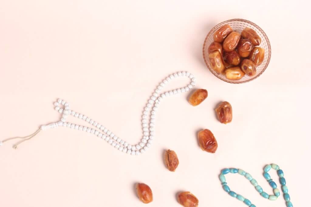 Dates in a glass cup surrounded by prayer beads.