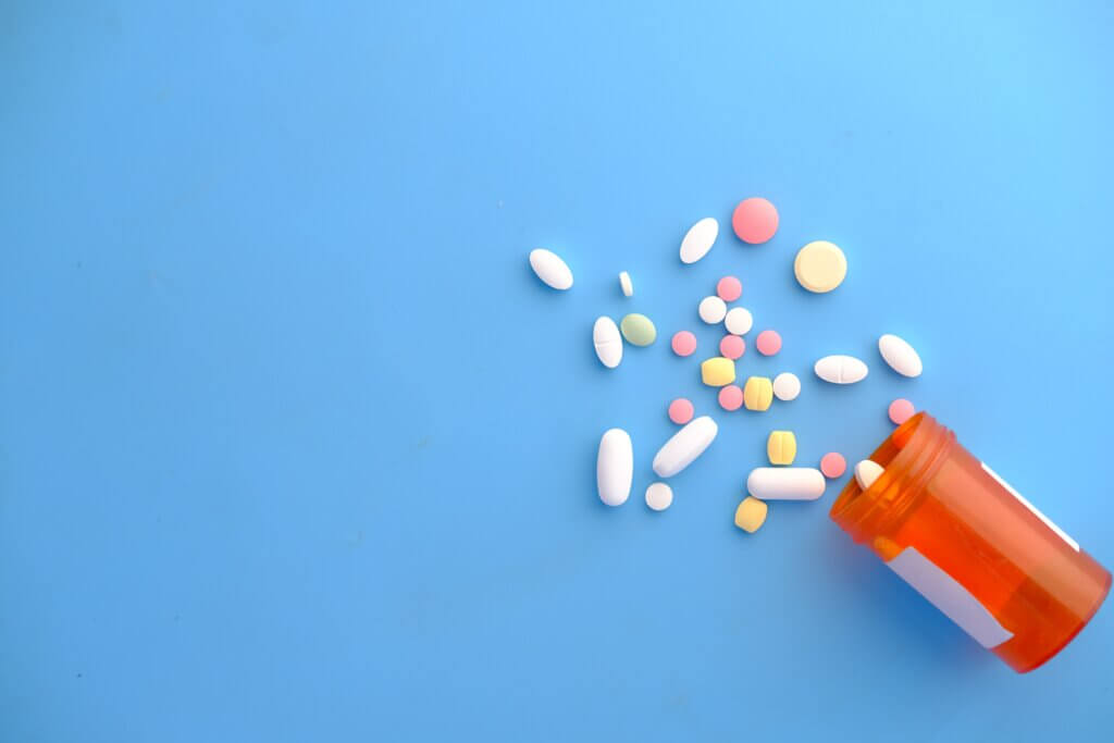 Pill bottle with different coloured pills against a blue background