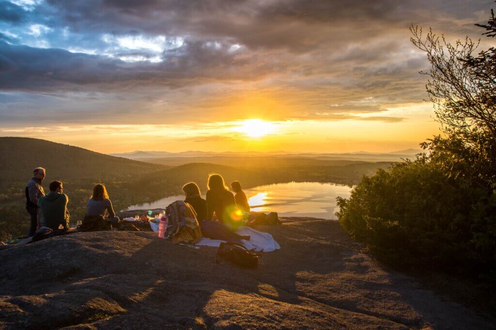 Folks sitting on mountain watching the sunset together