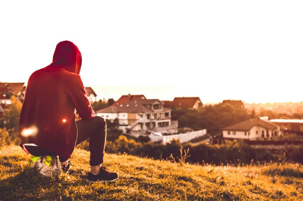 Individual sitting with back to camera on a hill watching the sunset