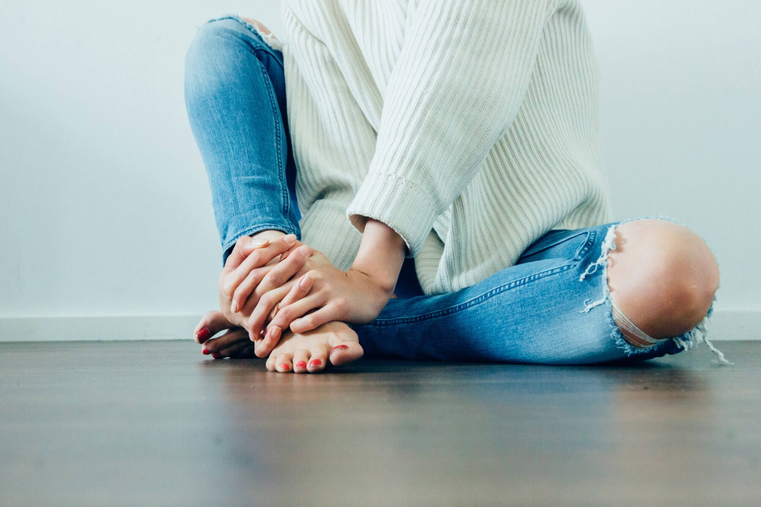 Shoulders down image of person sitting against a wall holding their foot in their hands