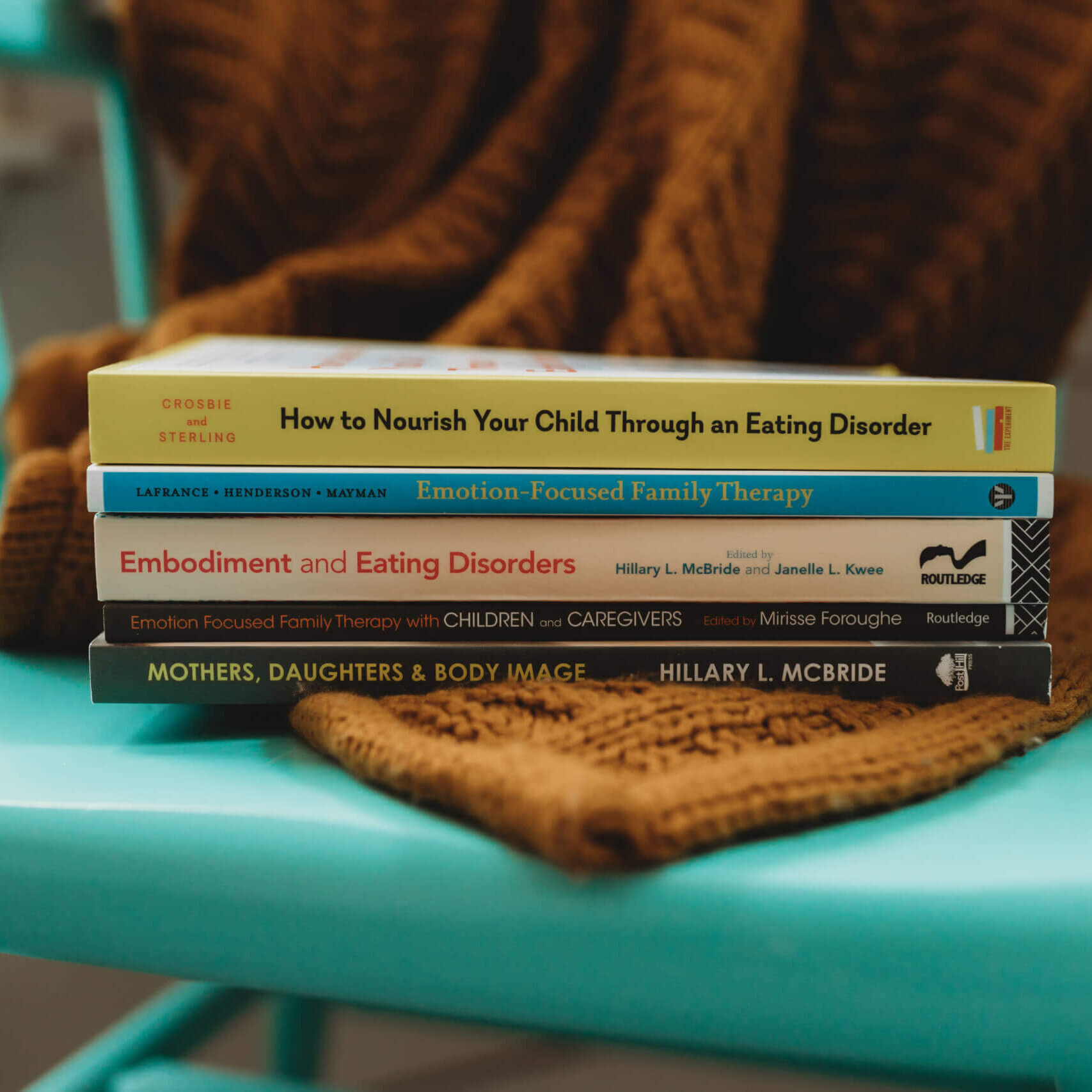 A stack of books about eating disorders is placed on a bright blue wooden chair.