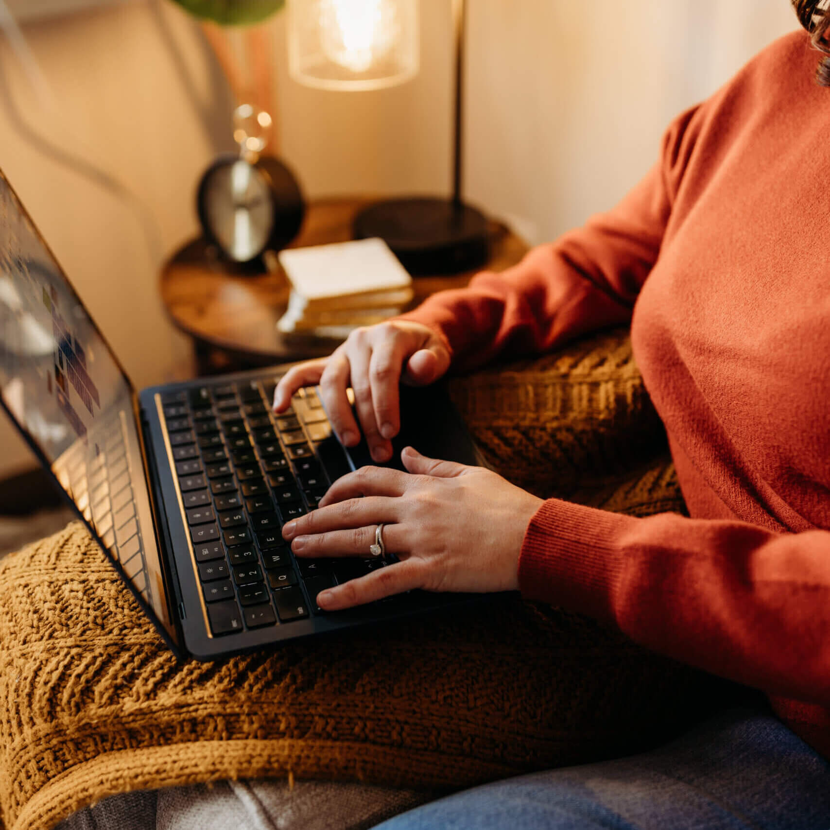 Someone wearing a red sweater typing on a laptop.