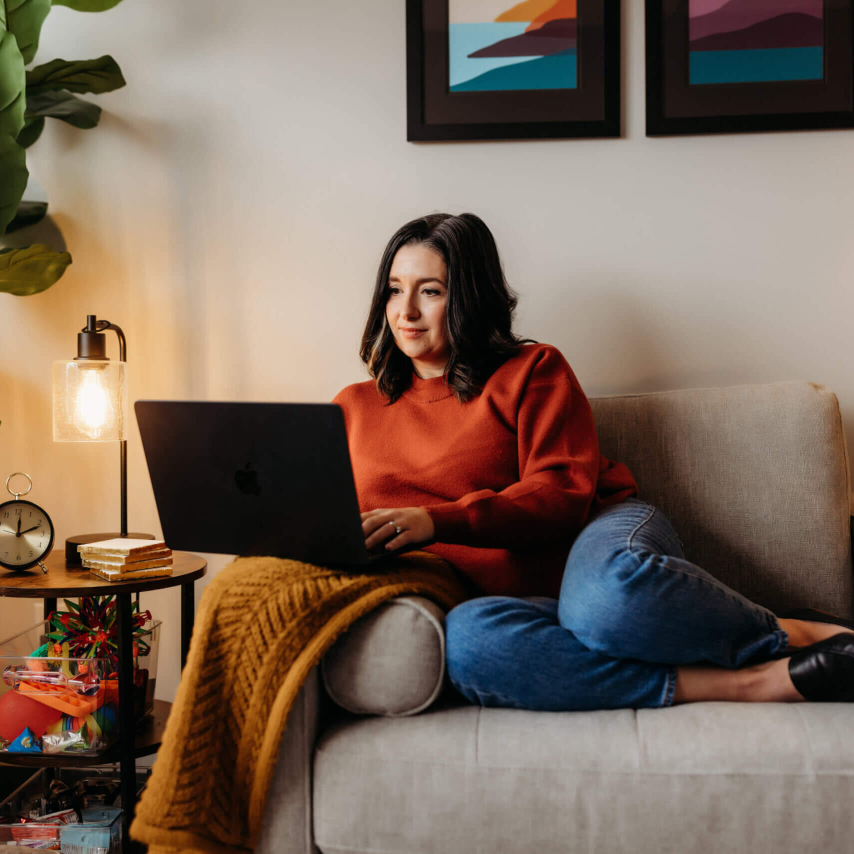 Person wearing red sweater sitting on a chair typing on a laptop.