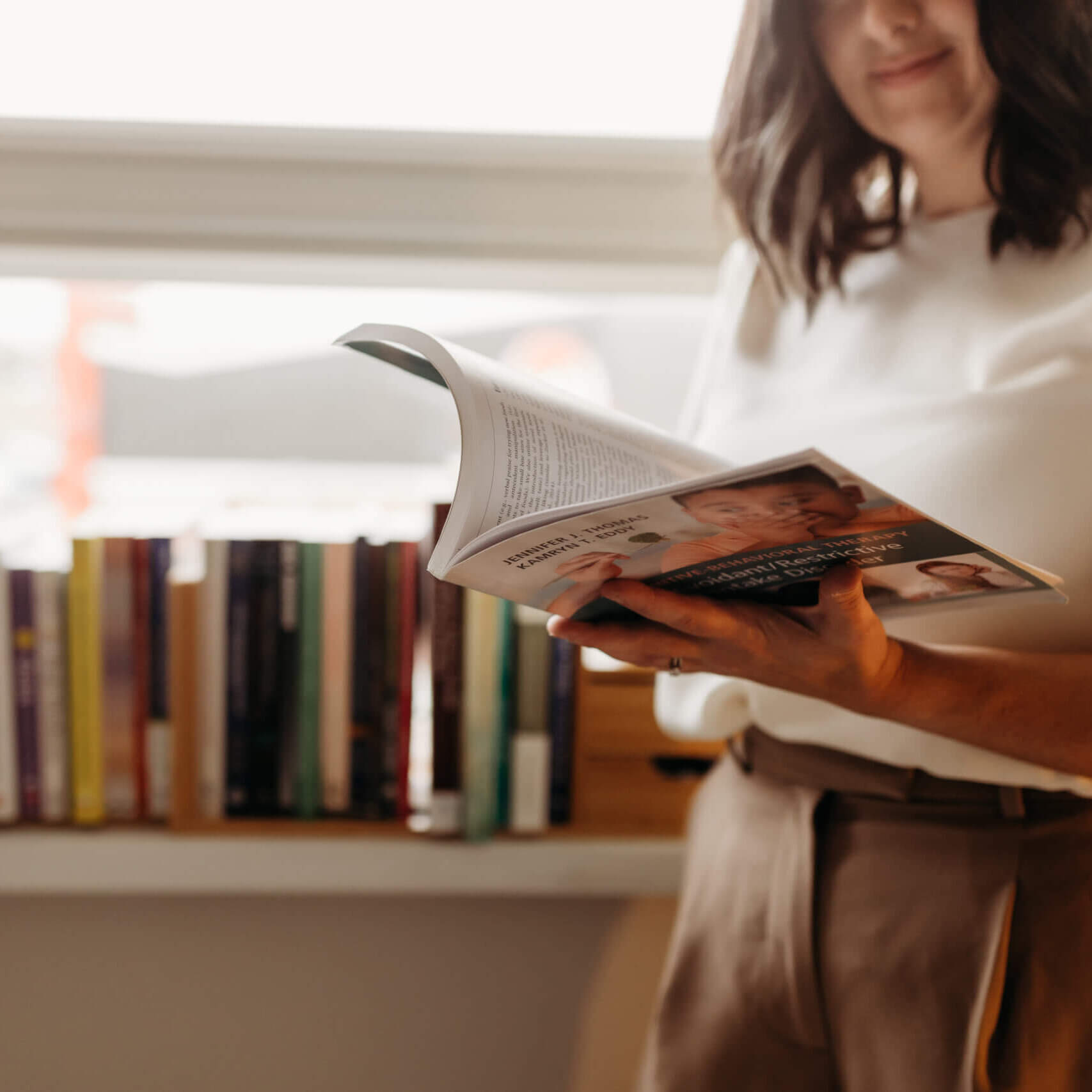 Jillian reading a book in front of a windowsill with books
