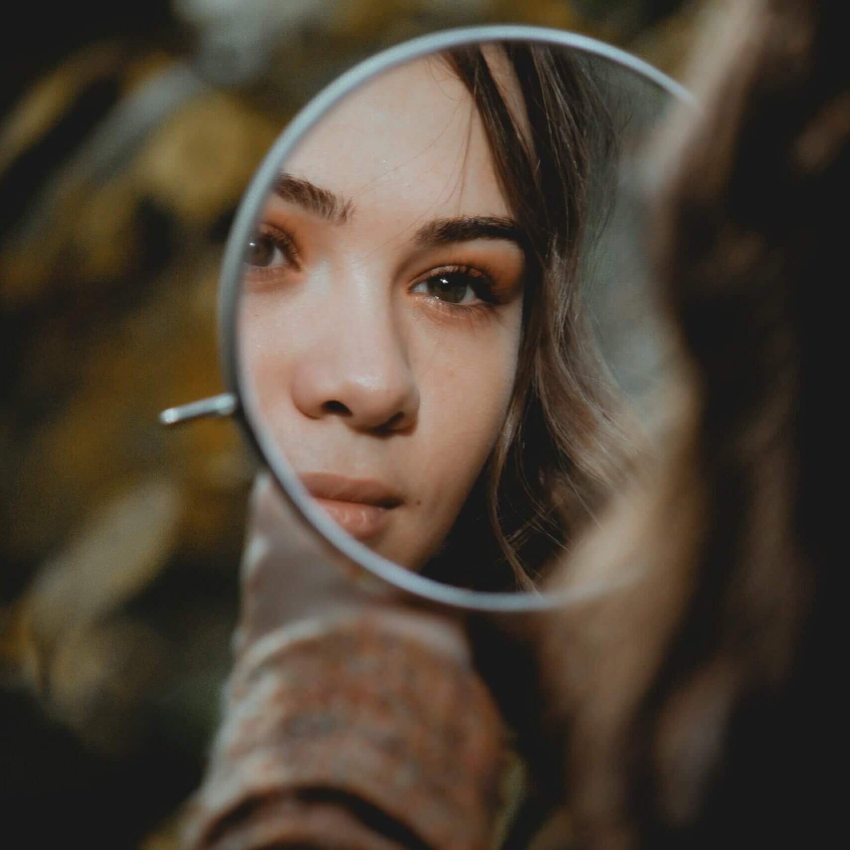 Someone looking at themselves in a small, rounds mirror